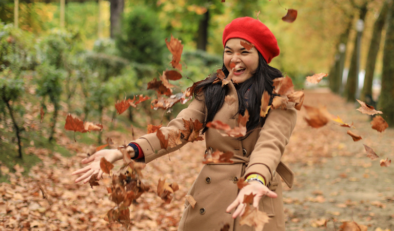 Woman with red hat throwing fallen autumn leaves in the air and smiling