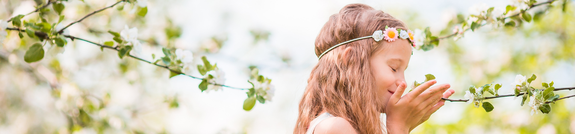 Little girl with flower headband on spring day smelling flowers