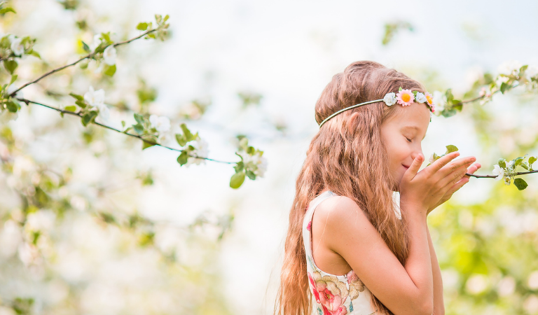 Little girl with flower headband on spring day smelling flowers